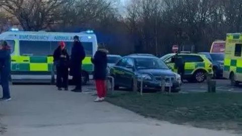 Ozgur Ontas Three ambulance vehicles can be seen in a car park with a few people milling about. 