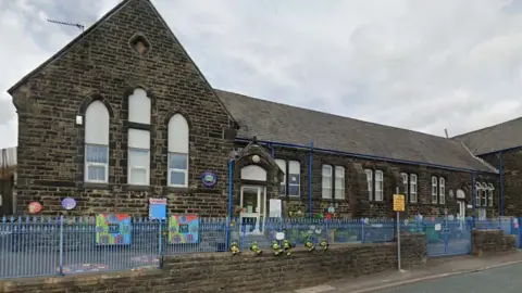 Google Street view image of Sharneyford Primary School in Bacup, a single storey  black stone building with blue metal railings and bright artworks on the front