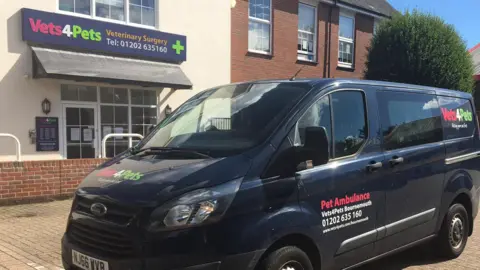 Dark blue van with pet ambulance branding parking outside a vets.