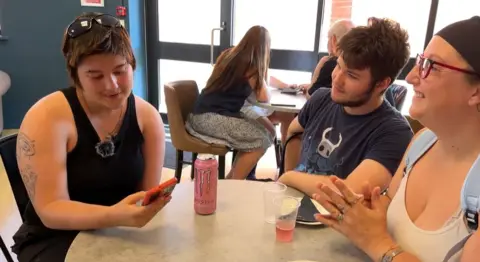 Three people sat around a table as one young person looks at a phone