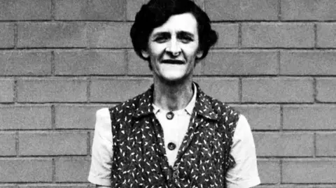 Steve Fielding Vintage photograph of Mabel Tattershaw, a dark haired middle aged woman, stood by a brick wall