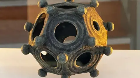 Norton Disney History and Archaeology Group A metal dodecahedron dating from the Roman times, it has cut out circles in the metalwork as well as small round balls of metal all over.  