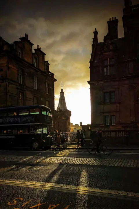 Colin Eaton A chink of sunlight through a gap in buildings. The buildings are dark and silhouetted against this bright light. 