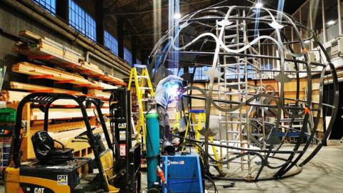 Man building a large ball-shaped metal frame 