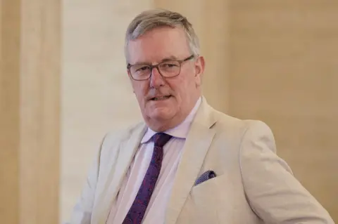 PA Mike Nesbitt in beige suit pink shirt and patterned purple tie