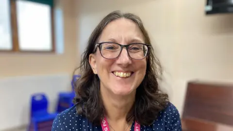 Deb Haddon is pictured smiling. She has brown hair and glasses. She is wearing a pink ID lanyard for the Ethereal Learning Foundation.  