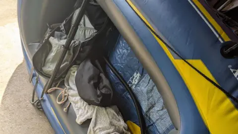 A blue and yellow dinghy with a unzipped rucksack, a white towel and black plastic tubing.