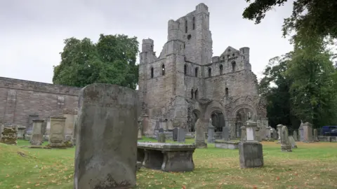 HES The historic Kelso Abbey - a ruined building on grassland with trees around it
