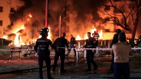 Emergency personnel standing in front of apartment building on fire in Tel Aviv