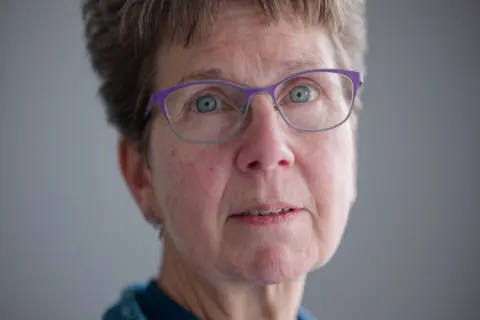 Laurence Cawley/BBC Judith Gibbons has short light brown hair, bright sea-blue eyes and purple rimmed glasses. 