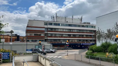 Sam Read/ BBC The outside of a five storey building with white and brown panelling with a zebra crossing outside the entrance. 