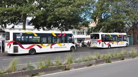 BBC Two white buses with red and yellow livery next to a bus terminus