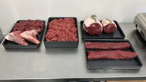 Leanne Rinne/BBC Large red pieces of venison meat are laid out on a table in a row including mince meat. 