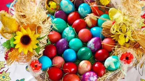 A basket of brightly painted Easter eggs surrounded by flowers