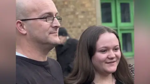 Brian Farmer/BBC A bald man wearing black glasses and a black, round-necked top next to a woman with long dark hair.