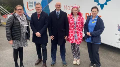 A group of five men and women huddle together outside a medical truck 