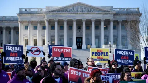 Getty Images People attend a rally of air traffic control and other airline industry unions on Capitol Hill in Washington, DC, on 10 January 2019 during the previous US government shutdown. People hold placards reading "Federal workers are American workers", "Stop the shutdown" and "Real people, real consequences".