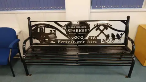 LDRS A black bench in an indoor setting which includes the words 'Mark Hillier' and 'Sparksy' as well as phrases such as 'Forever our hero'
