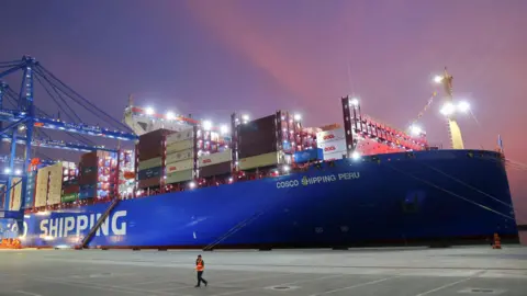 Reuters A man walks at China's state-owned Cosco Shipping Chancay port inaugurated during the APEC Summit, in Chancay, Peru. There is a large container ship framed by a colourful sunset. 