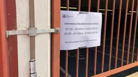 Alex Pope/BBC A sign on red railings at a car park.