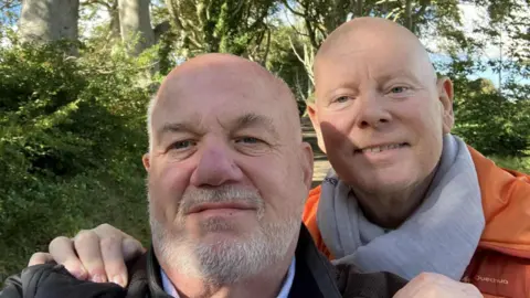 Two men looking at the camera, one has a white beard