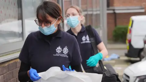 PA Media Two forensics officers at the scene, entering Imtech House on Woodthorpe Road in Ashford, Surrey