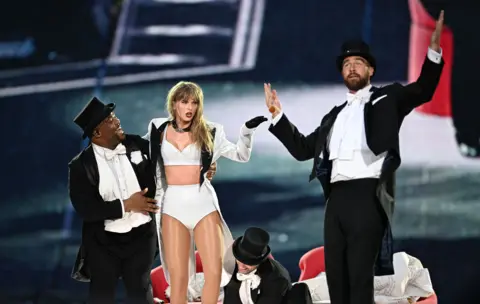 Getty A dancer, Taylor Swift and Travis Kelce on stage. 