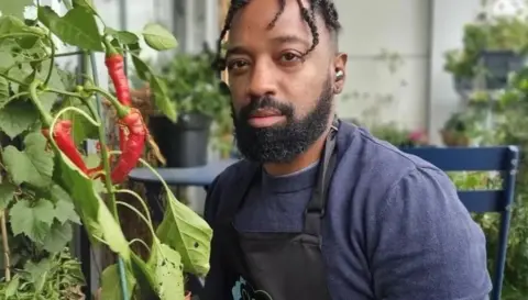 Jason Williams is sitting on his balcony surrounded by a variety of different plants.