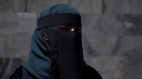 Safia, with her face covered, in a classroom stood in front of a wall