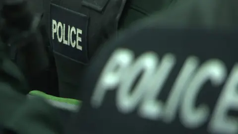 A close-up of the back of two police officers wearing black jackets with the word police in white on them