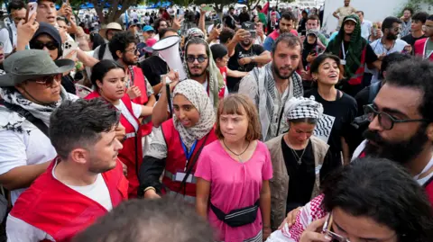Reuters Crowds of people, wearing red hi-vis jackets and traditional scarves associated with the pro-Palestine movement surround Greta Thunberg at port Sidi Bou Said. 