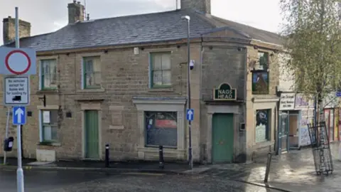Street view image of the Nag's Head pub. A stone building on a street corner with green windows and doors and a sign in black with gold wording over the door, which is on the corner, that says NAG'S HEAD