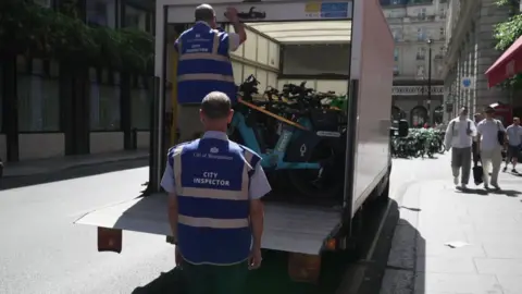 Two people load hire e-bikes into the back of a white van.