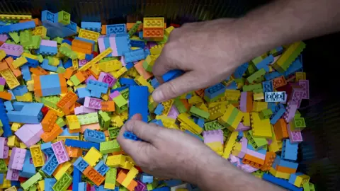 PA Media A person's hands can be seen in a pit of multi-coloured lego bricks.