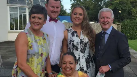 Family handout Dressed for a formal event, Candy is wearing a multi-coloured dress as she sits down. Behind her, starting from the left hand side is Jill wearing a flowered dress, a man wearing a white shirt and red bow tie, a woman wearing a black and white dress and then Jill's husband wearing a black suit with a blue shirt with a black tie.