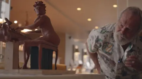 Terry Gilliam leans down to get a closer look at the small maquette version of the Terry Jones sculpture