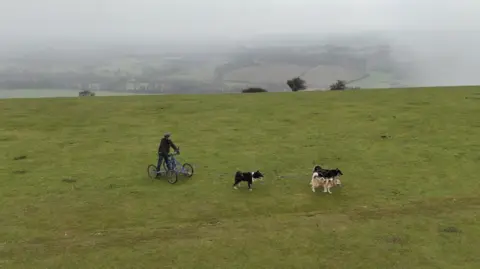Matt Hodgson on a four-wheeled, aluminium kart, pulled by three husky dogs on the top of Firle Beacon on the Sussex Downs.