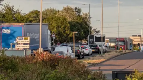 Carol Moring A long line of traffic queuing along a dual-carriageway road. A man is pictured in the background, having got out of his car in the queue.