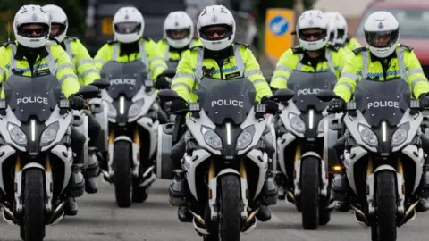 PA Media Um grupo de policiais montando motos. Todos estão usando capacetes brancos e jaquetas de alta visita.