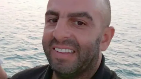 LNER Samir Zitouni is smiling at the camera in a close-up shot of his face. he is balding and has a moutache and a beard