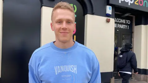 A man standing in Redditch town centre, wearing a blue jumper.