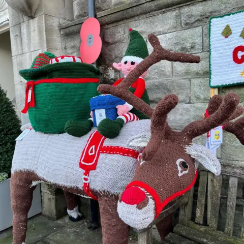 Suzanne Excell A knitted reindeer faces the camera, with a knitted elf and sack of toys on its back