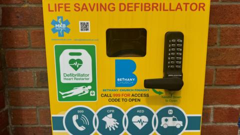 The defibrillator on a red brick wall at Bethany Church