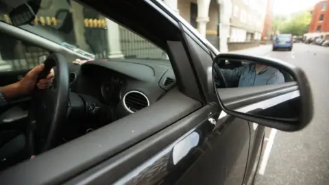 PA Media A driver viewed through the wing mirror of his black car is shown not to be wearing a seat belt