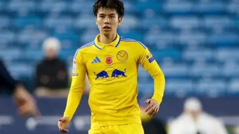 Leeds United FC Ao Tanaka wearing the yellow Leeds United shirt to be auctioned during Leeds' match against Millwall on 6 November