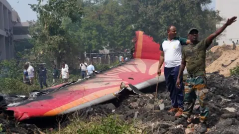 Two people stand gesticulating by a part of the downed Air India aircraft wreckage