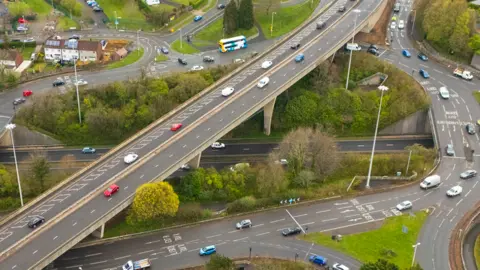 A traffic interchange with three levels and vehicles on the roads with greenery in between the roads.