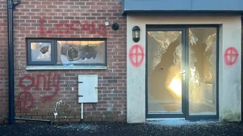 BBC The picture shows the boarded up windows of a house with what are either cross-hairs or cross symbols painted on the walls 