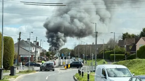 Essex Fire and Rescue Service smoke billows from a home in the distance with streets and cars in the foreground