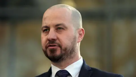 PA Media Det Ch Insp Nick Gardner: The head and shoulders of a man with short dark hair and a dark beard wearing a blue jacket, plain shirt and blue tie. He is looking to his right.